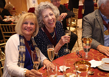 Two women smiling at a planned giving celebration dinner. Links to Gifts by Will